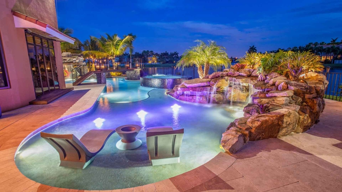 a swimming pool with a rock waterfall and LED lights at night - Van Kirk & Sons Pools & Spas a swimming pool with a rock waterfall and LED lights at night