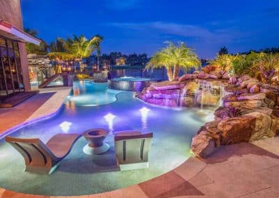Tropical-themed pool with waterfall, night lighting, and lush greenery.