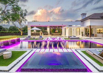Modern luxury backyard with custom LED pool, spa, fire features, and outdoor kitchen in South Florida