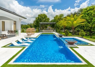 Luxury modern inground pool with in-water loungers, raised spa, and fire bowls by Van Kirk & Sons.