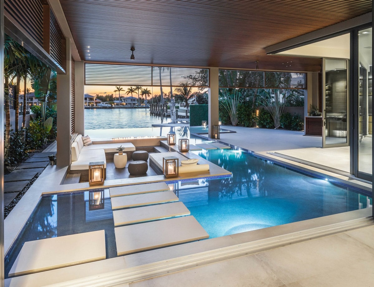 Luxurious indoor-outdoor pool area with elegant seating and waterfront view at sunset.