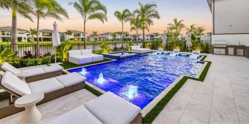 Luxury outdoor pool area with lounge chairs and palm trees at sunset.