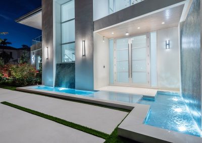 Modern house entrance with illuminated acrylic water fountain features and frosted glass doors at night.
