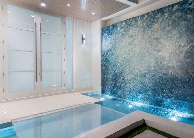 Luxury indoor pool area with modern waterfall feature and frosted acrylic glass doors in a sleek, elegant design.
