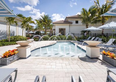 Luxurious poolside with fountains, palm trees, and lounge chairs under shade on a sunny day.