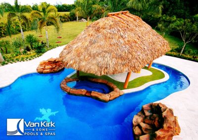 Luxury lazy river pool with tiki hut and rock features in tropical garden setting.