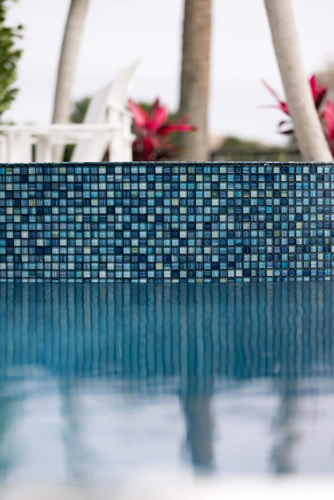 Sparkling blue mosaic pool tiles with palm trees in the background, creating a serene outdoor oasis.