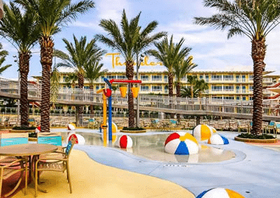 Tropical resort pool with palm trees and colorful beach balls under a clear sky. Relaxing vacation spot.