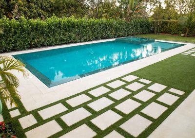 Classic backyard pool with geometric tile design surrounded by lush greenery.