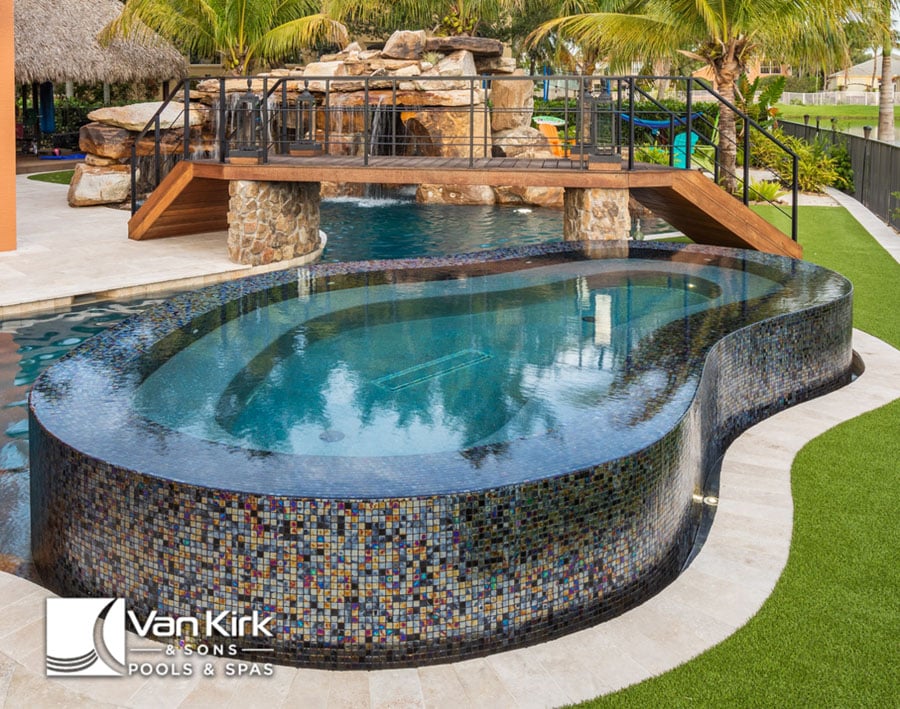 Luxury pool with mosaic tiles, waterfall feature, and tropical landscaping, designed by Van Kirk & Sons Pools & Spas.