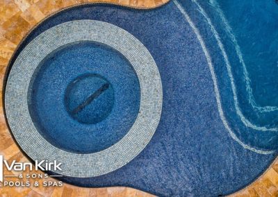 Circular blue tiled hot tub with adjacent pool, surrounded by brown stone tiles from Van Kirk & Sons Pools & Spas.