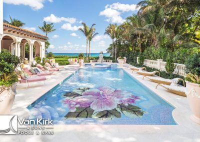 Luxurious floral mosaic tile pool with pink lounge chairs, palm trees, and ocean view at Van Kirk & Sons Pools & Spas.