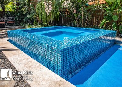 Modern blue-tiled spa with water feature in landscaped garden setting, designed by Van Kirk & Sons Pools & Spas.