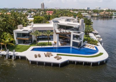 Luxury waterfront mansion with modern design, infinity pool, and palm trees overlooking a serene lake.