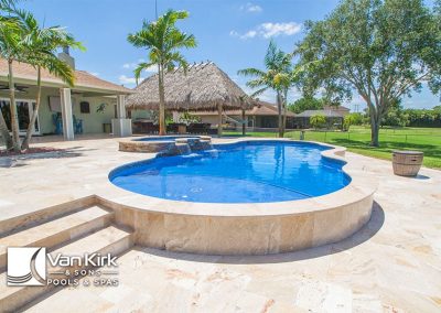 Luxurious backyard pool with tiki hut and palm trees on a sunny day, designed by Van Kirk & Sons Pools & Spas.