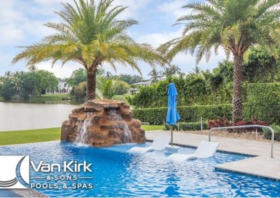 Luxurious pool with waterfall, palm trees, and lounge chairs by Van Kirk & Sons Pools & Spas. Relaxing outdoor oasis.