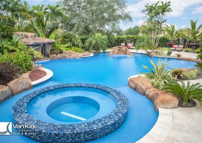 Luxurious backyard lagoon pool with spa, surrounded by tropical plants and vibrant greenery.