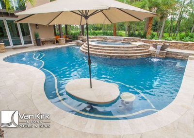 Luxury backyard freeform style pool with spa, umbrella, and waterfall feature surrounded by tropical landscaping.