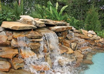 Natural stone waterfall cascading into a turquoise pool surrounded by lush greenery.