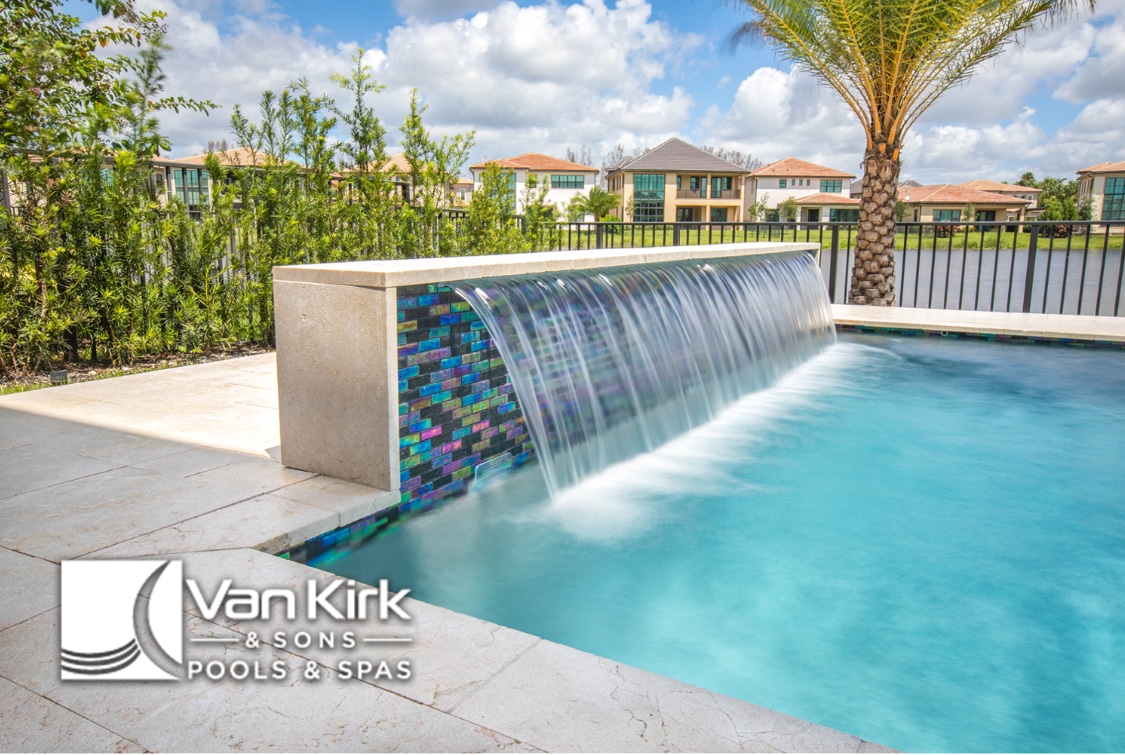 Luxury pool with cascading waterfall feature, surrounded by lush greenery and modern houses in the background.