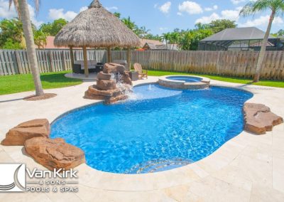 Tropical pool with waterfall and tiki hut in a sunny backyard, designed by Van Kirk & Sons Pools & Spas.