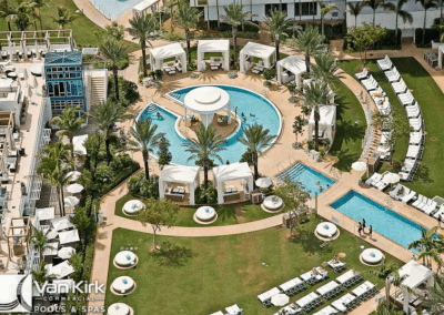 Aerial view of luxury resort pool with cabanas, palm trees, and sun loungers, creating a relaxing tropical atmosphere.