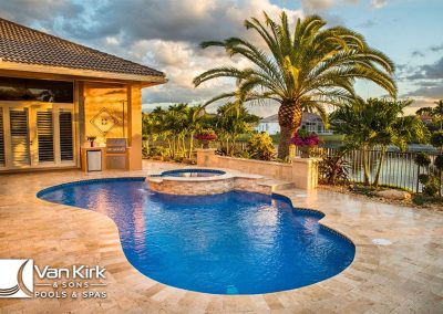 Luxurious backyard free form pool and spa with palm trees at sunset near a lake by Van Kirk and Sons Pools & Spas.