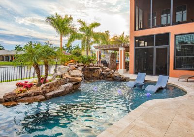 Luxury backyard freeform pool with waterfall, palm trees, and lounge chairs, perfect for a tropical retreat.