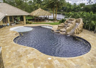 Luxury outdoor pool with waterfall slide, tiki hut, and lush landscaping by a serene lake. Ideal for relaxation.