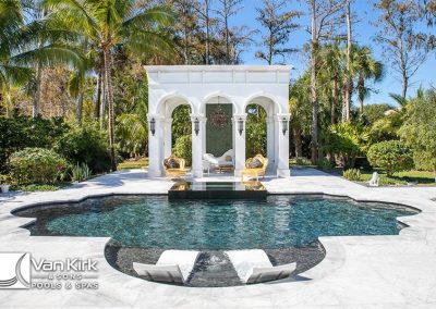 Luxurious roman style backyard pool with elegant white gazebo, surrounded by tropical trees and lounge chairs.