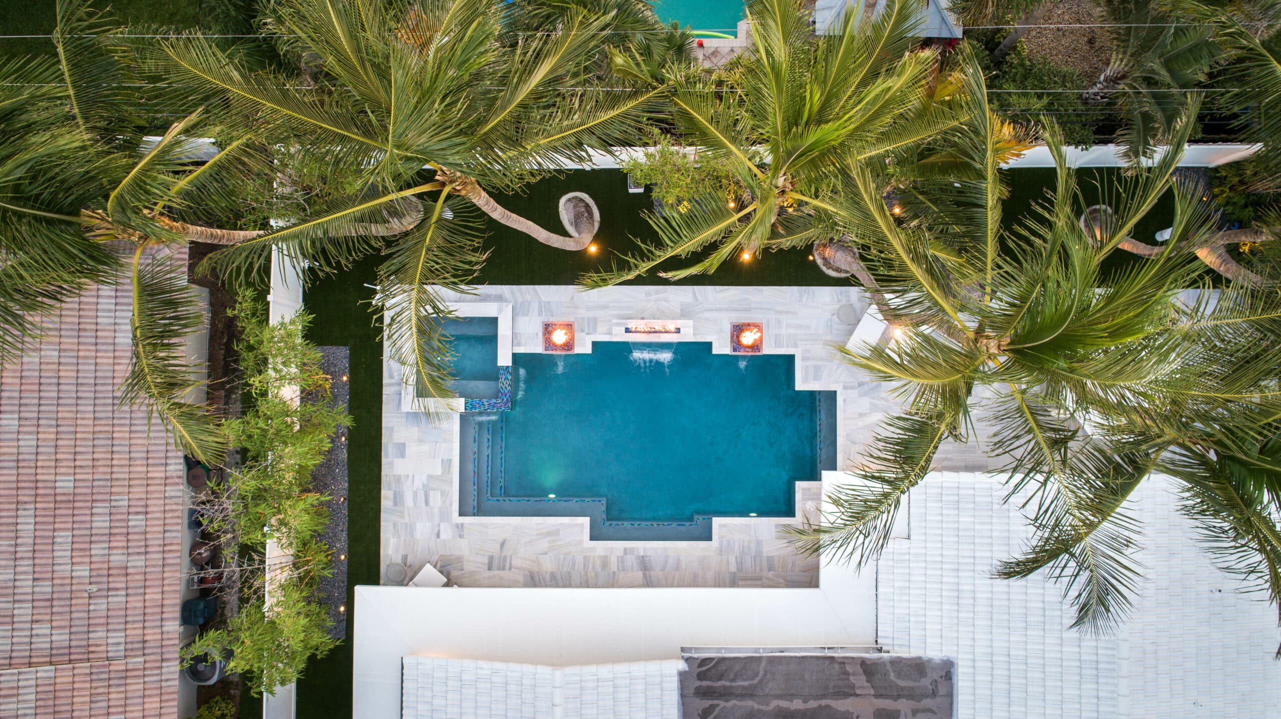 Aerial view of a luxury backyard geometric pool surrounded by palm trees and modern patio design.