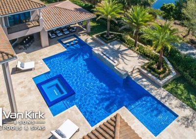 Luxurious backyard roman style pool with spa, surrounded by palm trees and a tiled patio. Perfect for relaxation and entertaining.