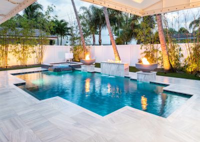 Luxurious backyard, geometric pool with fire features and palm trees, perfect for relaxation and entertainment.
