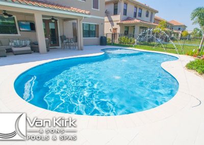 Backyard with custom lagoon shaped swimming pool by Van Kirk & Sons, surrounded by patio furniture and greenery.