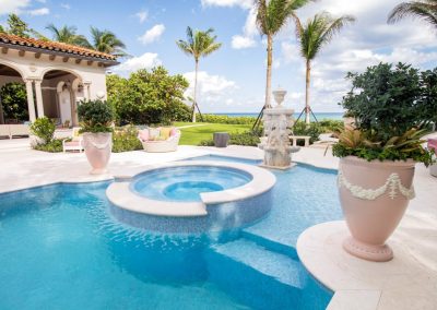 Luxurious backyard pool and hot tub with ocean view, surrounded by palm trees and elegant patio decor.
