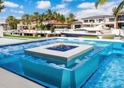 Luxurious pool and spa with fire feature, palm trees, and boats under a sunny blue sky, creating a tropical paradise feel.