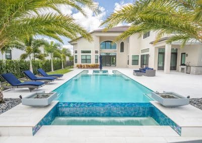Luxury modern house with a palm-lined backyard and a sparkling infinity swimming pool, lounge chairs, and outdoor seating area.