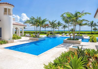 Luxury beachfront villa with palm trees, pool, and ocean view under a clear blue sky. Perfect tropical getaway.