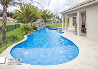 Luxurious freeform style pool with stone accents and lush landscaping, next to a modern patio area in a residential setting.