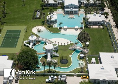 Luxurious backyard with lazy river pools, a tennis court, and landscaped gardens by Van Kirk & Sons Pools & Spas. Aerial view.