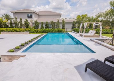 Luxurious backyard with a modern straight pool, sun loungers, and a shaded cabana, surrounded by lush greenery.