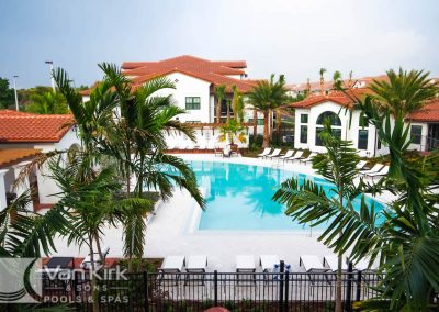 Luxury resort pool surrounded by palm trees and loungers, with a view of Spanish-style architecture in the background.