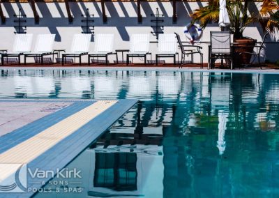 Outdoor pool with lounge chairs and palm trees, perfect for relaxation by Van Kirk & Sons Pools & Spas.