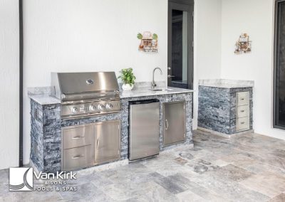 Outdoor kitchen with stainless steel grill and sink on a stone countertop, ideal for backyard entertaining.