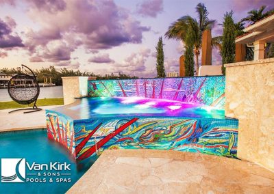 Vibrant mosaic infinity pool with colorful lights at sunset, created by Van Kirk & Sons Pools & Spas.