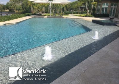 Luxury backyard pool with bubbler fountains and modern design, surrounded by lush greenery and a seating area.