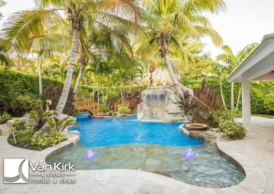 Lush tropical backyard lagoon style pool with waterfall and palm trees, designed by Van Kirk & Sons Pools & Spas.