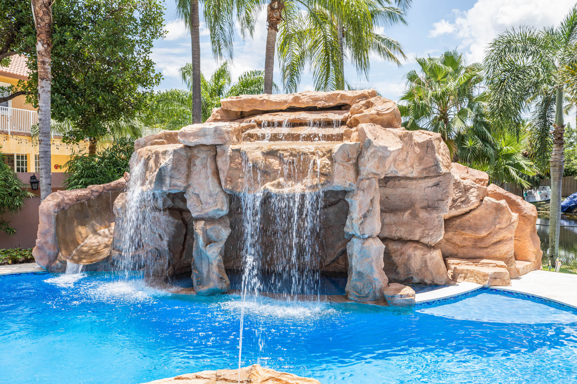 Tropical pool waterfall with rock formations and lush palm trees on a sunny day.
