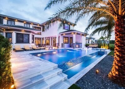 Luxurious modern home with an infinity pool, palm trees, and elegant outdoor lighting at dusk.