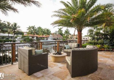 Patio with wicker chairs and palm tree overlooking canal, offering a serene waterfront view and fire pit. Perfect for relaxation.